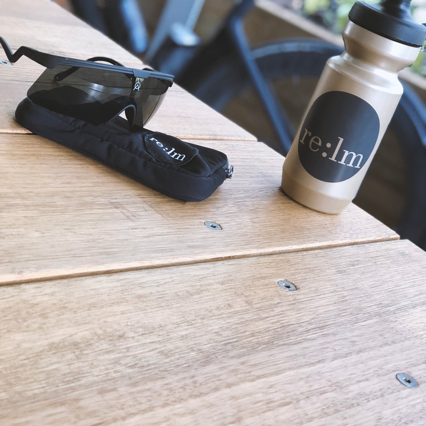 Black cycling pocket pouch, gold bidon and Alba Optics sunglasses on table.