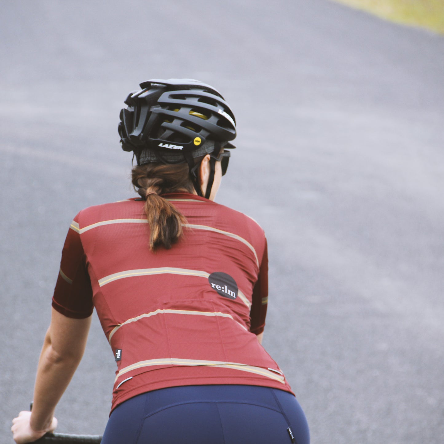 Woman riding bike wearing Relm Cycling jersey in offset design and Lazer helmet